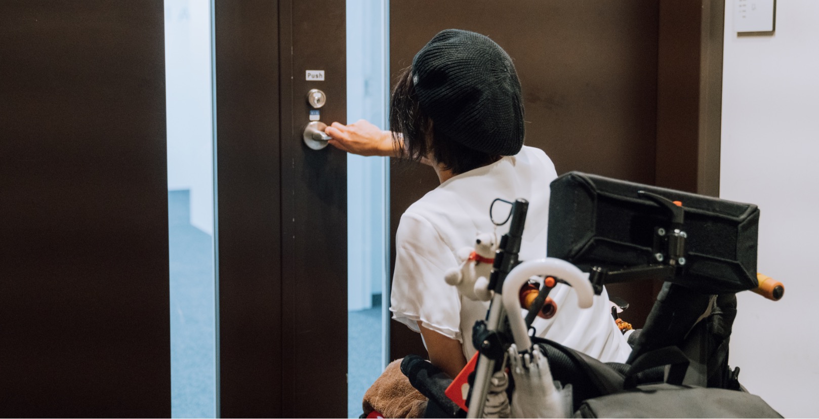 リードユーザーの和久井さんが車椅子に乗ってドアを開けようとしている写真