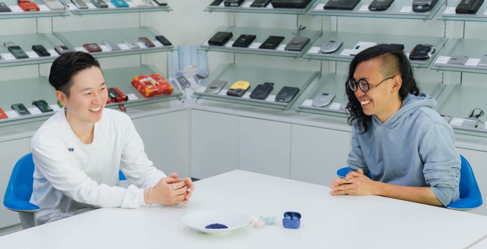 本坊健一郎さんと加藤功将さんが、再生プラスチックを用いた素材を手元に、向かい合って座り、視線は合わせずにお互い笑っている写真。