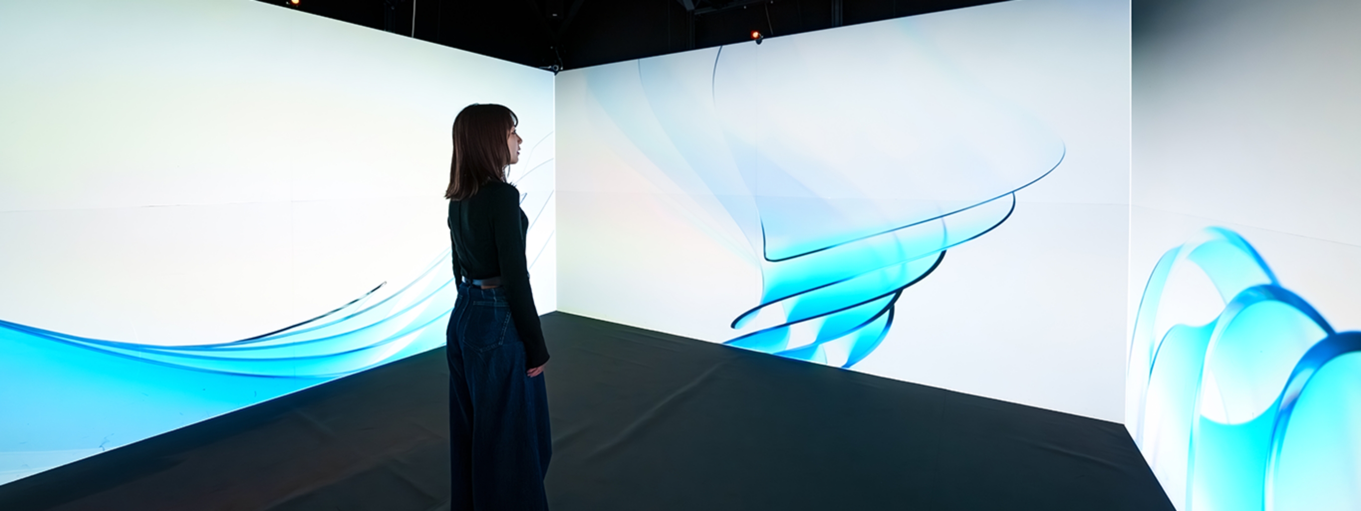 イマーシブスクエアを使用し、壁3面のマルチディスプレイに画像を投影されているのを見ている女性