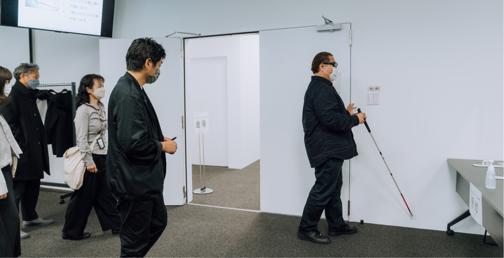 会議室の壁を触り白杖でドアを探している佐藤 尋宣さんの写真