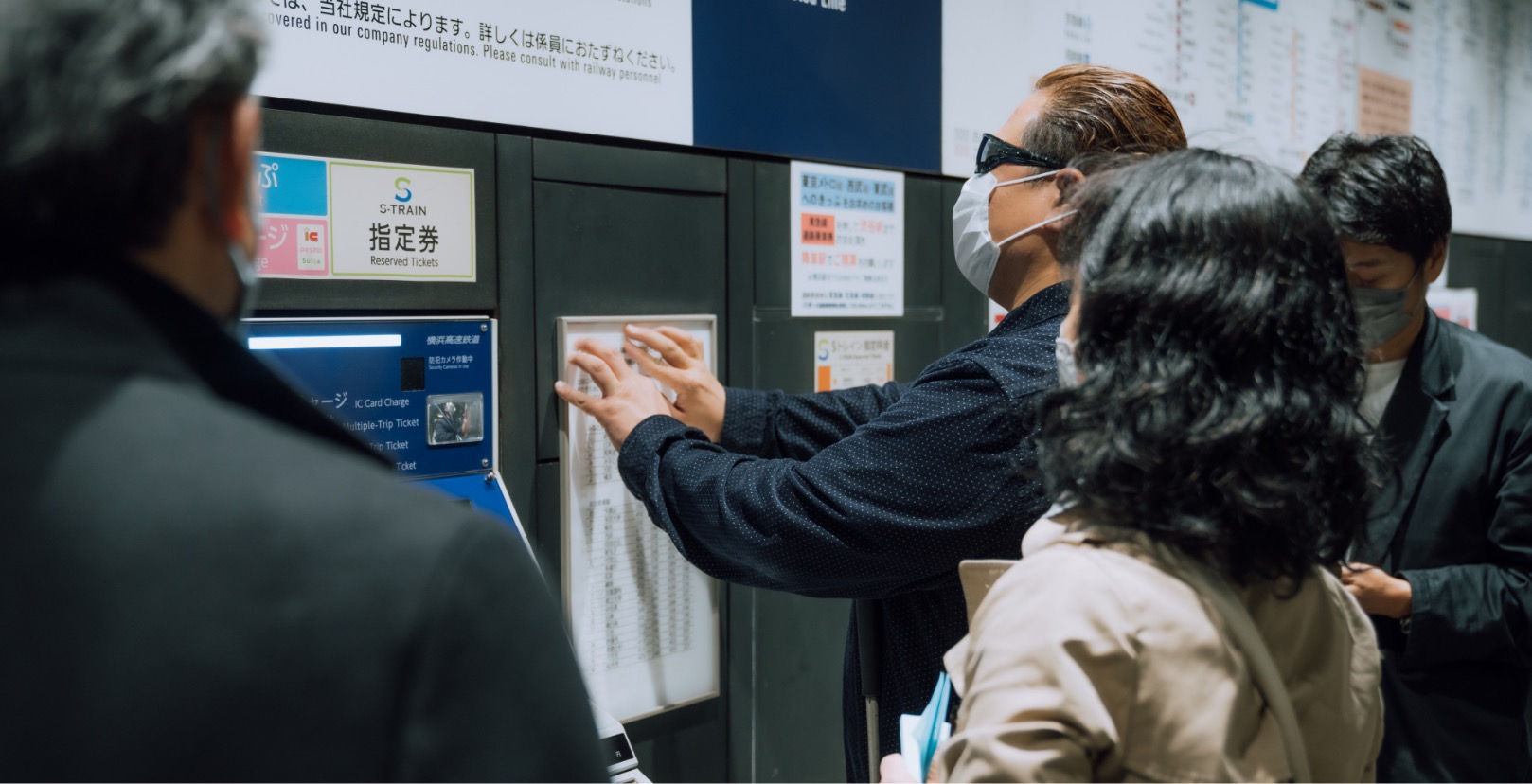 佐藤 尋宣さんが切符売り場の料金表を触っている写真