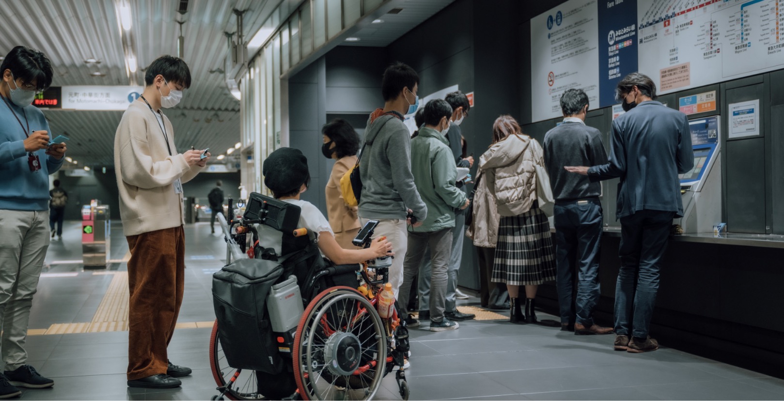 リードユーザーの和久井さんが駅の切符売り場で列に並んでいる写真