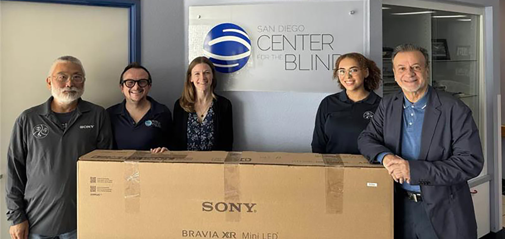 San Diego Center for the Blindのサインの前でブラビアの箱を囲むメンバーたち