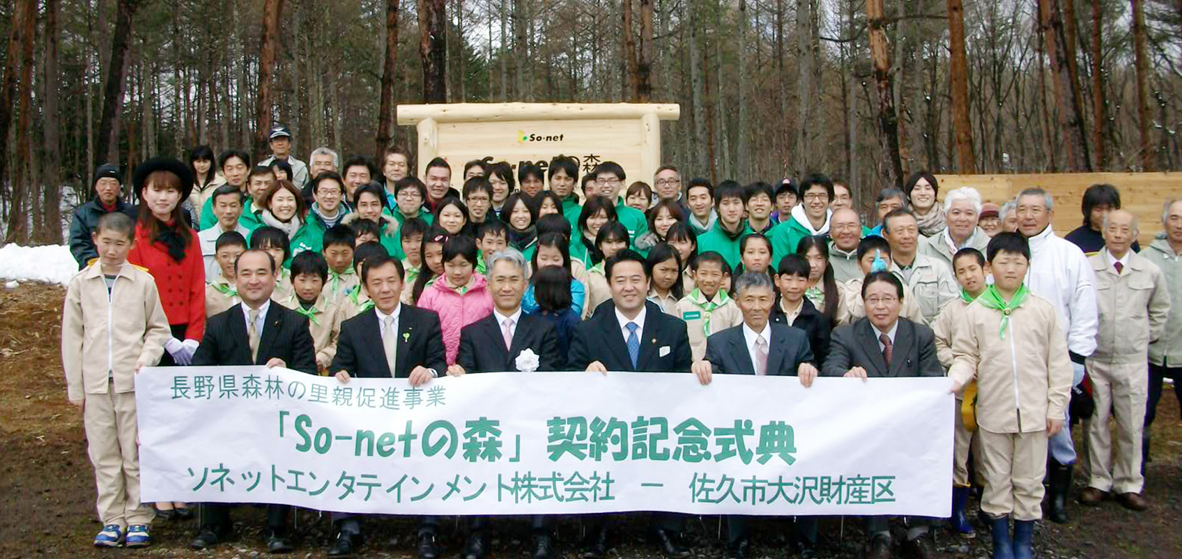 木の看板の前で参加者が集合しており、「So-netの森」と書かれた横断幕をもっている
