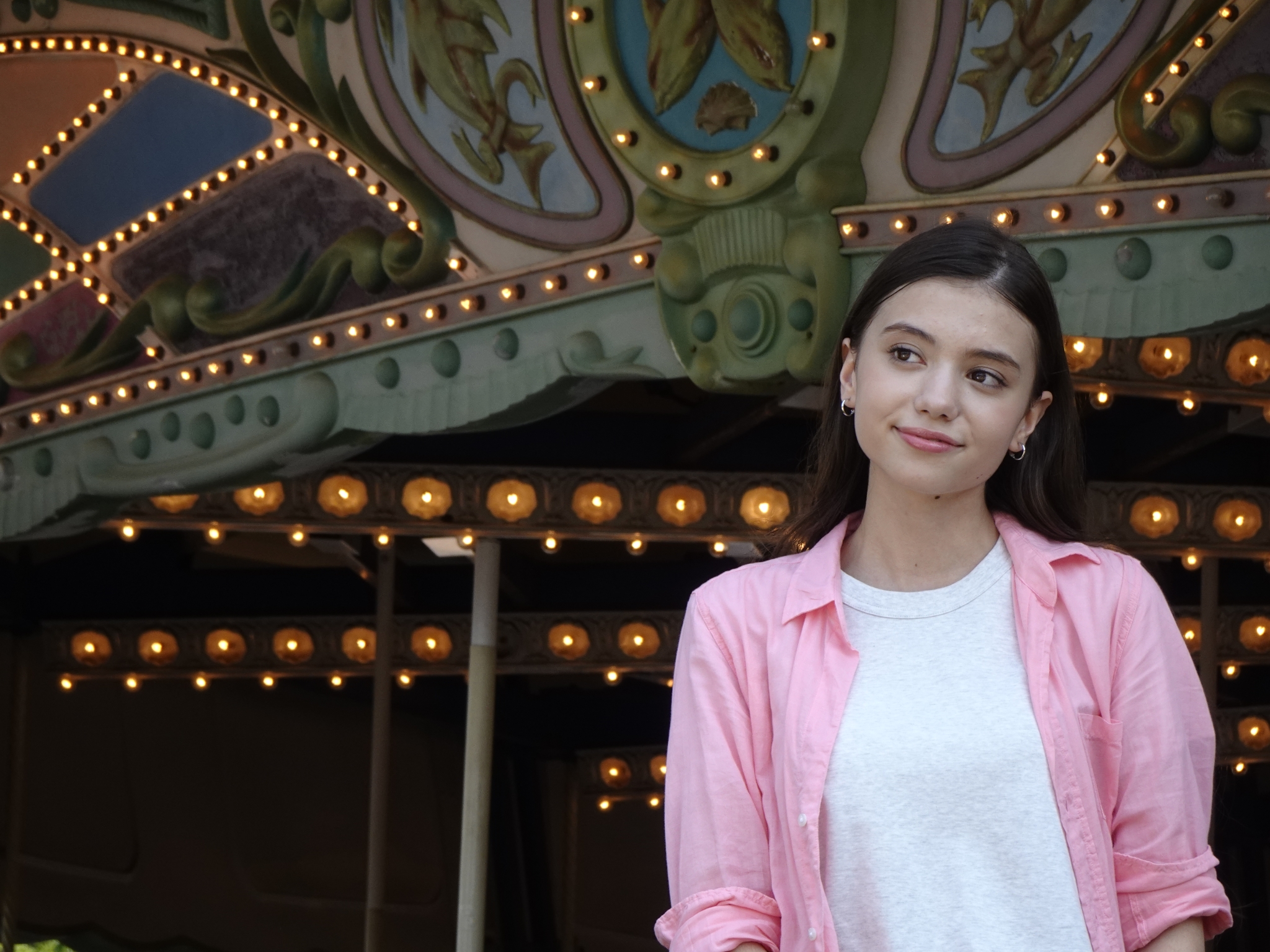 Portrait of female model looking to her right, a fairground ride the background Click to open modal