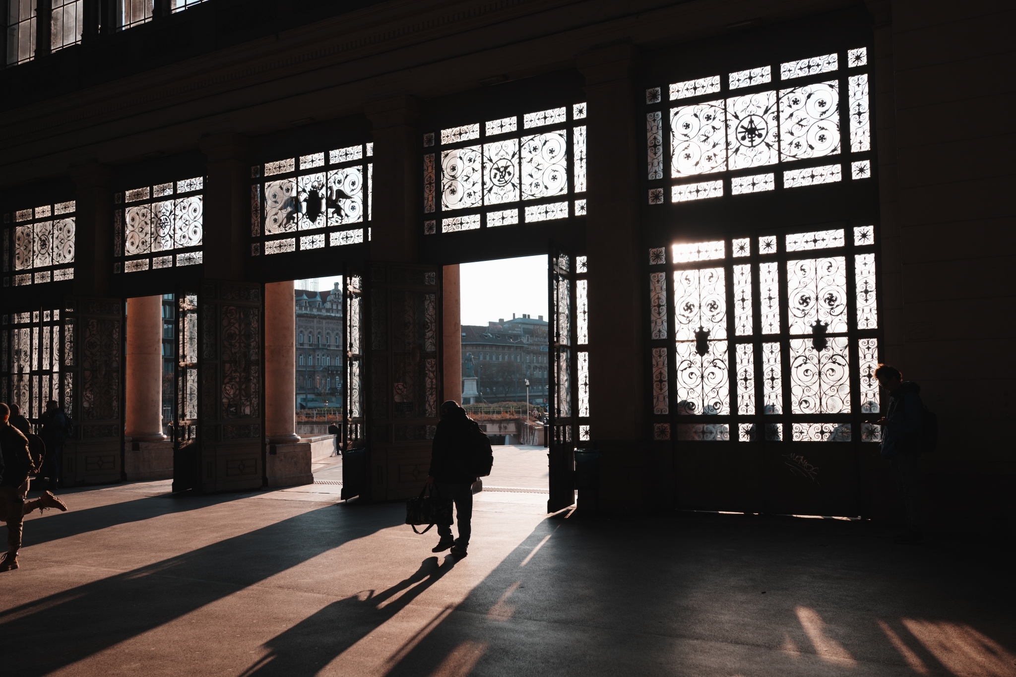 A sample image of a man walking outside a building with sunlight streaming in from outside, showing his back and elongated shadows, talen by Creative Look FL3 mode. Click to open modal