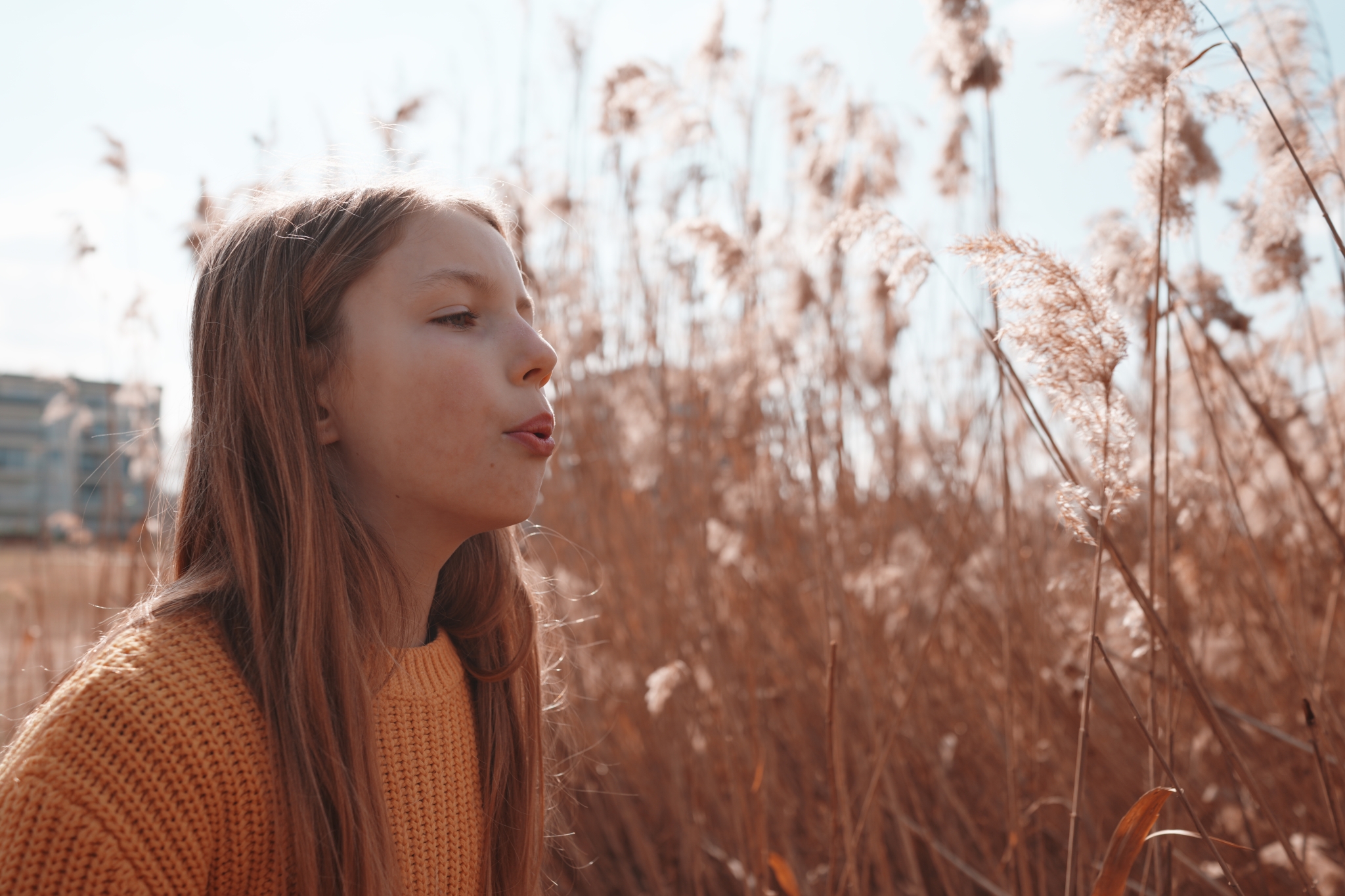 A sample image of a girl blowing on pampas grass, taken in Creative Look FL3 mode. Click to open modal