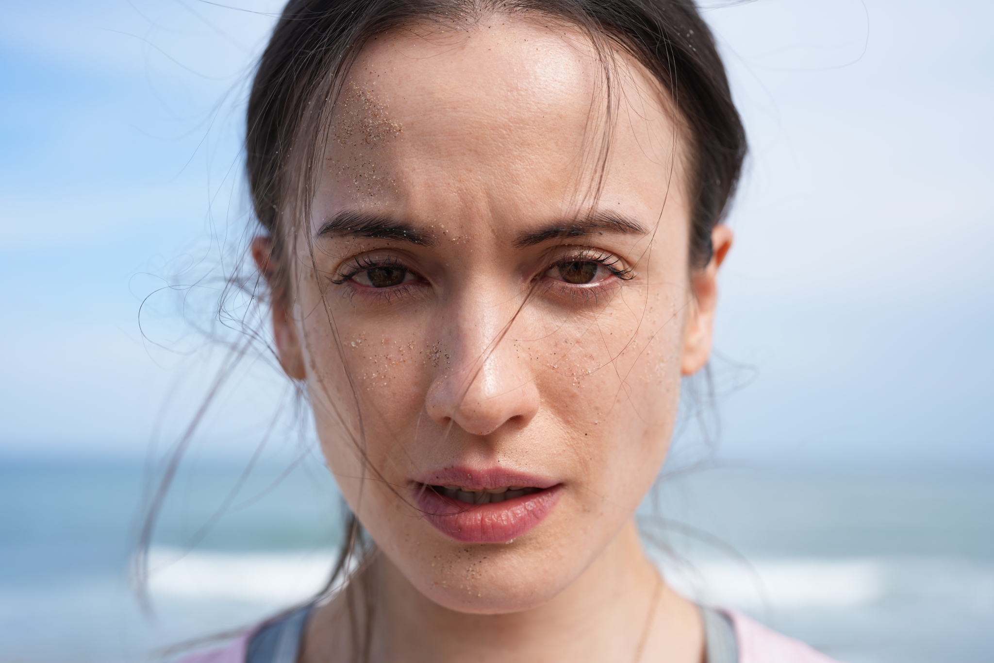 Close-up of a woman's face showcasing skin texture with ocean in the background Click to open modal