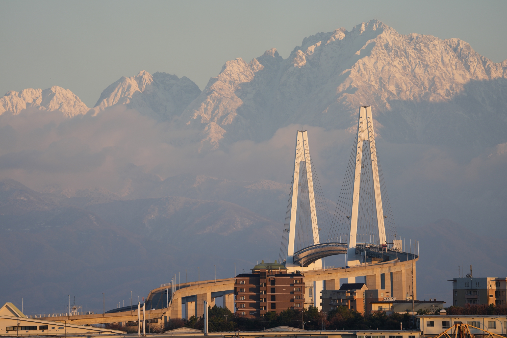 A bridge with snow-covered mountains in the background at sunrise. Click to open modal