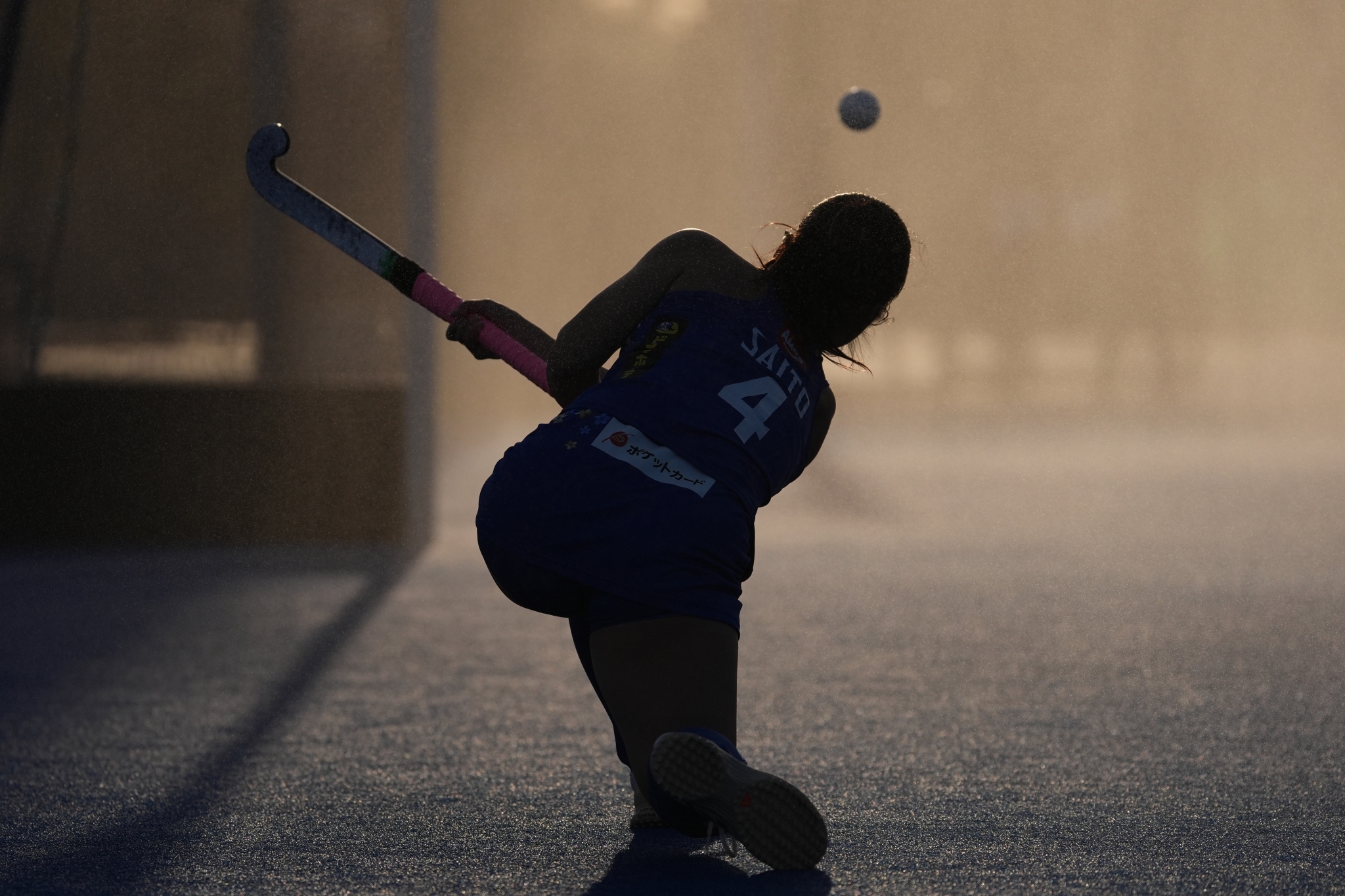 Silhouette of a field hockey player hitting a ball in the sun. Click to open modal