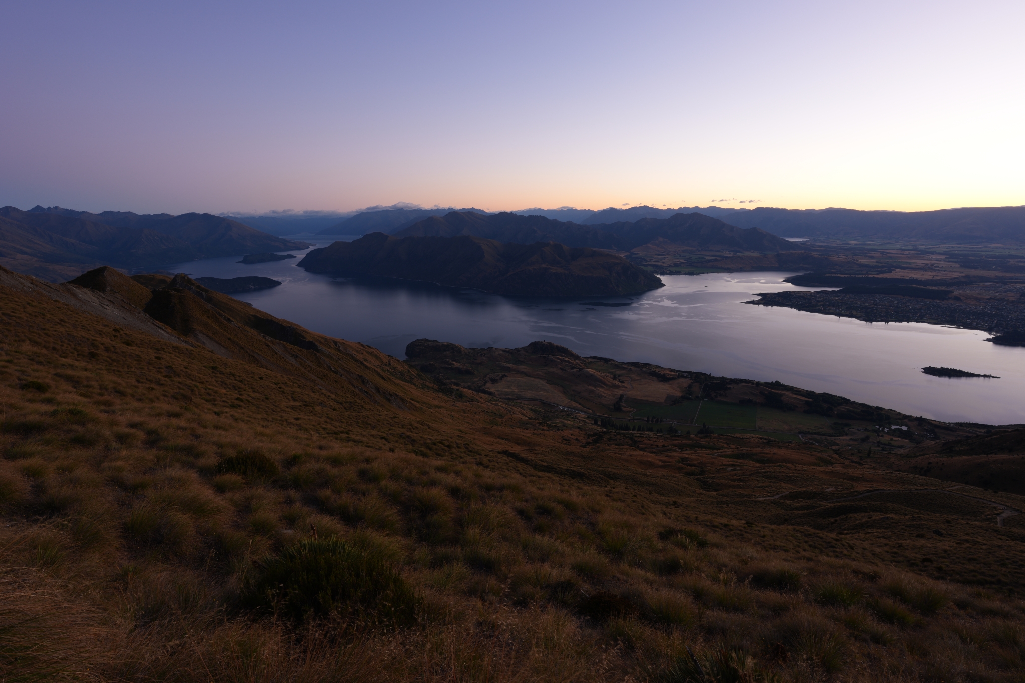 A landscape photo of a lake and layered terrain viewed from a hill at dusk Click to open modal