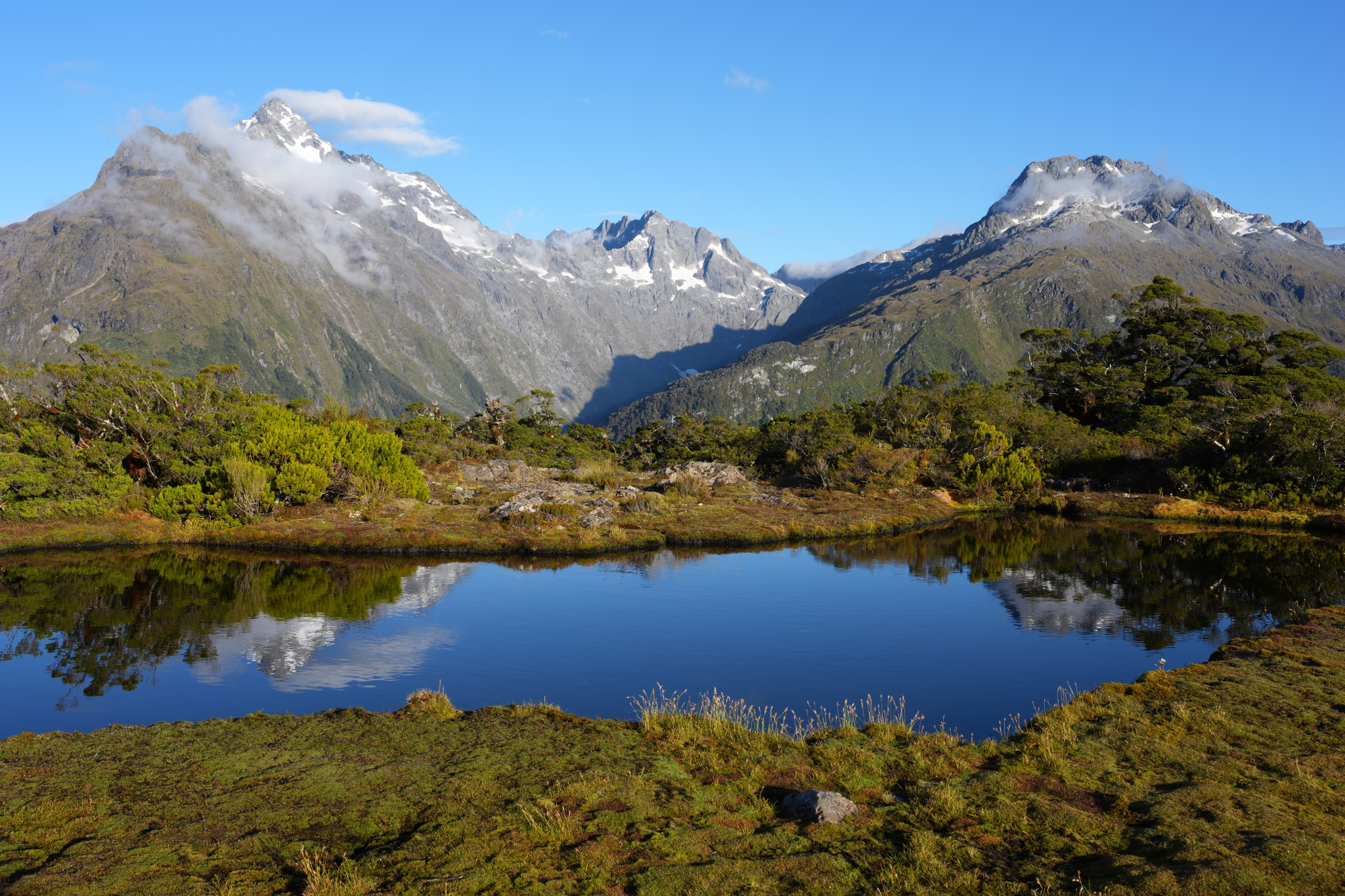 A landscape photo of a lake quietly reflecting surrounding mountains and forests Click to open modal