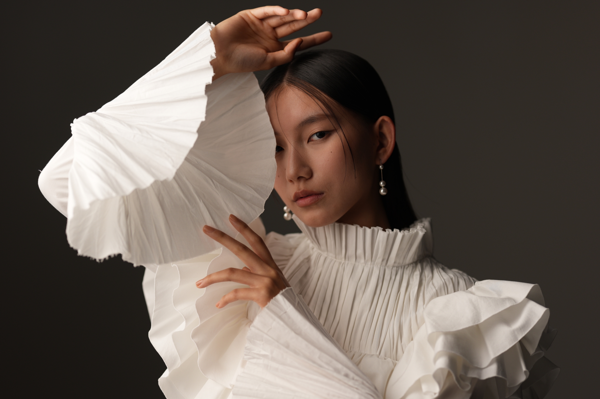 A portrait of a woman wearing white clothing, posing with her arms raised Click to open modal