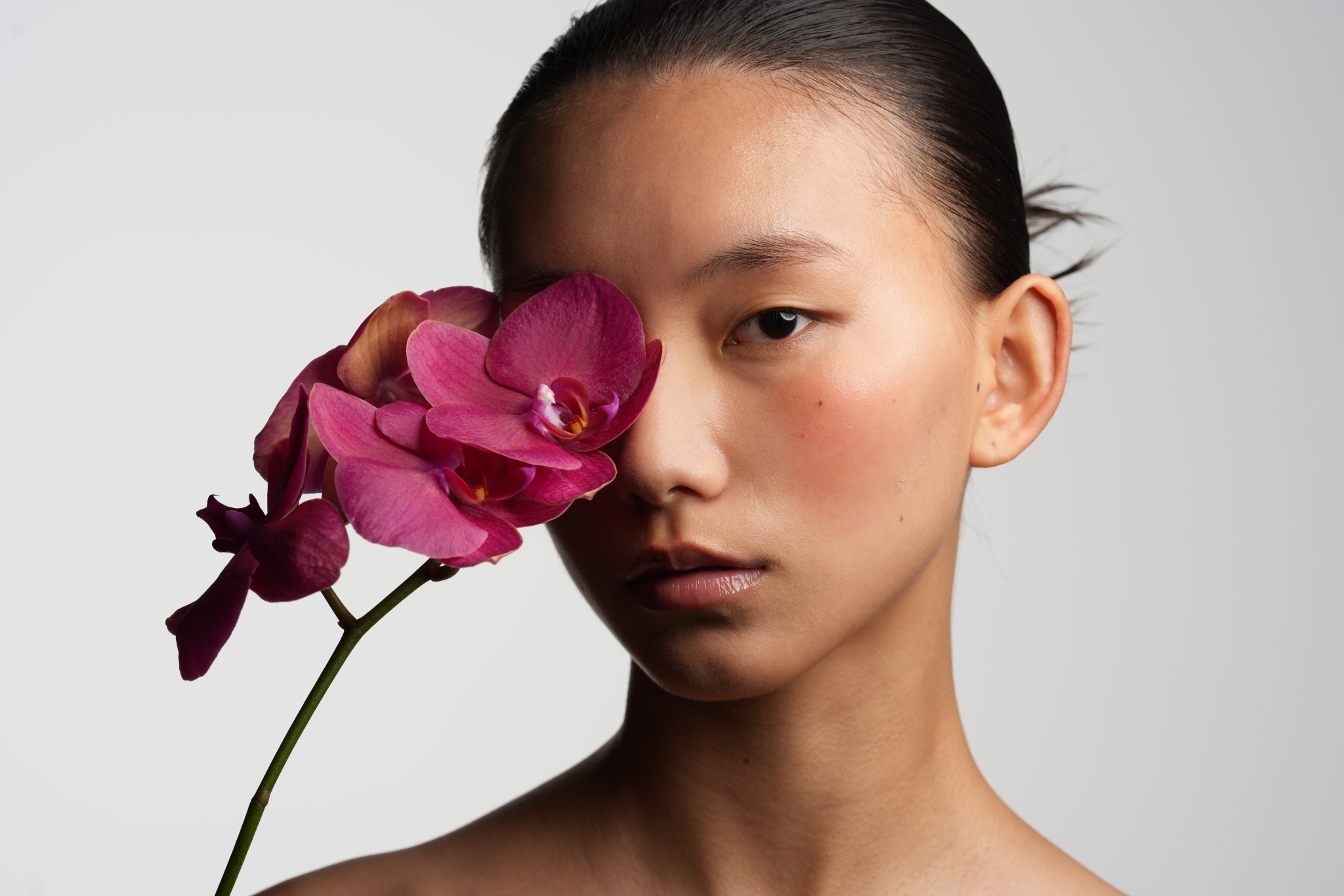 A portrait of a woman holding a pink flower in front of her face Click to open modal