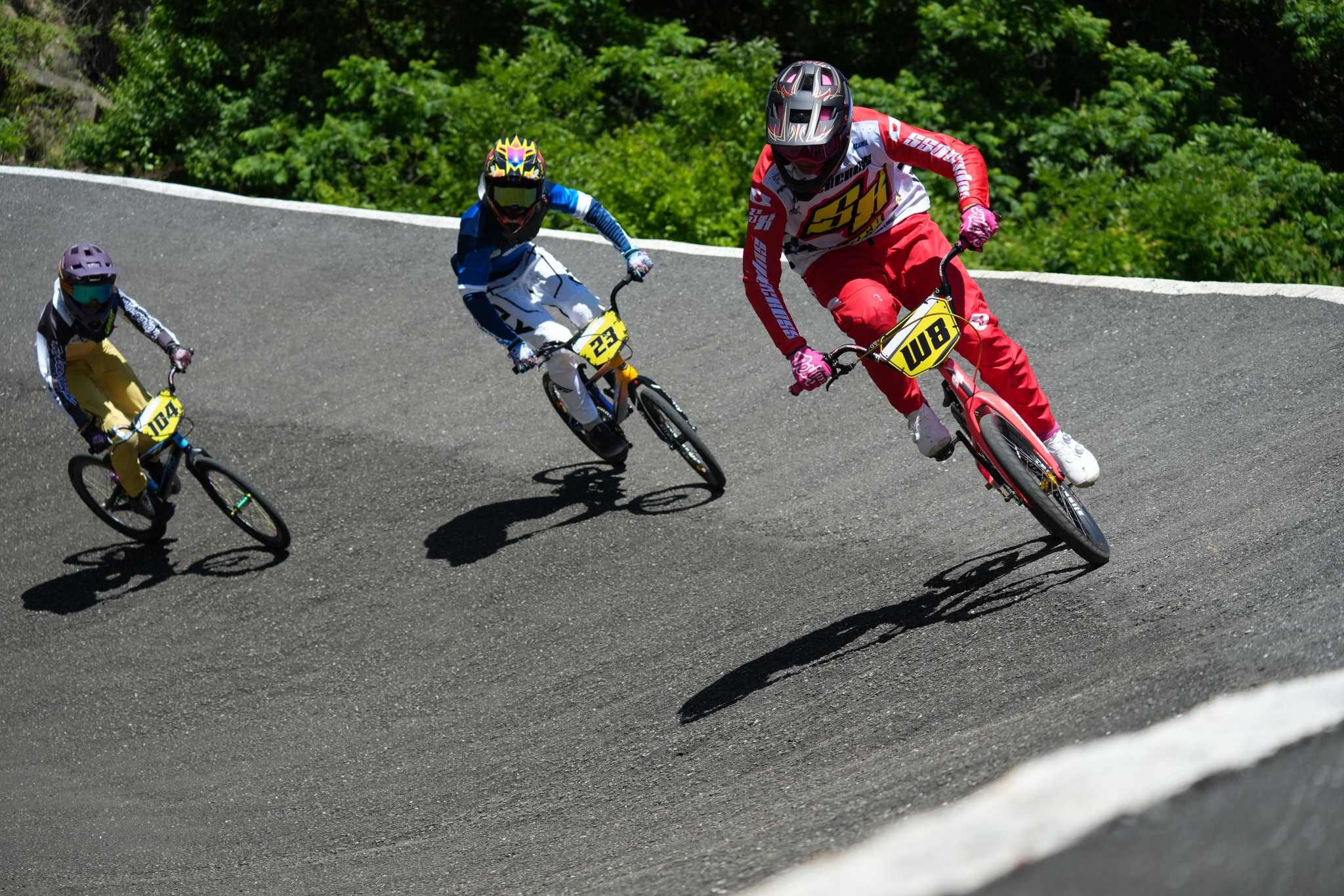 Three BMX racers speeding around a curved track. Click to open modal