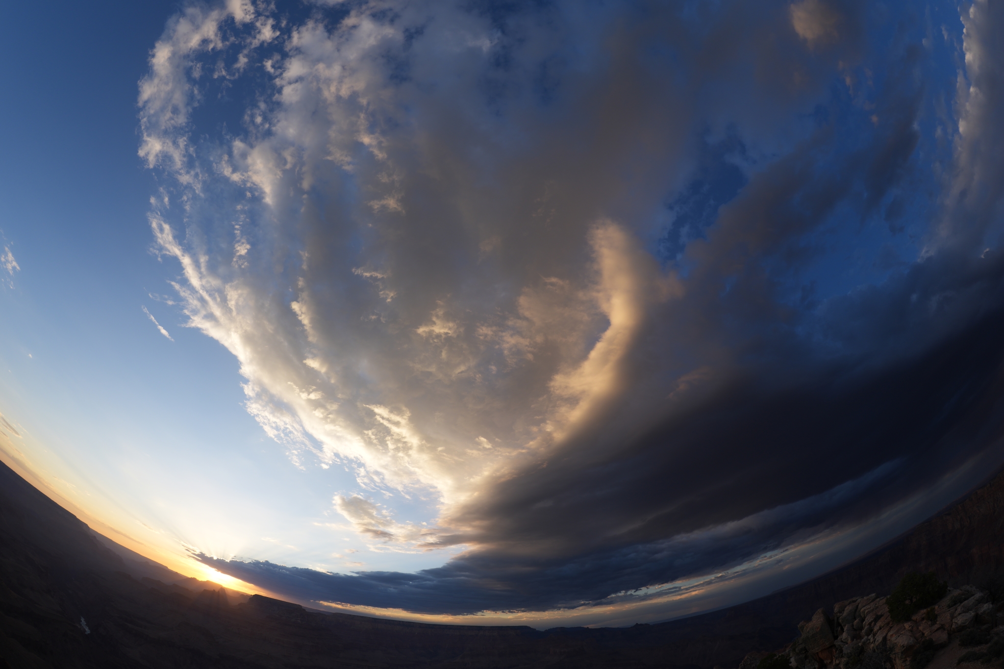 Fisheye lens view of sky and land meeting at curved horizon with dramatic cloud formations and golden and blue lighting Click to open modal