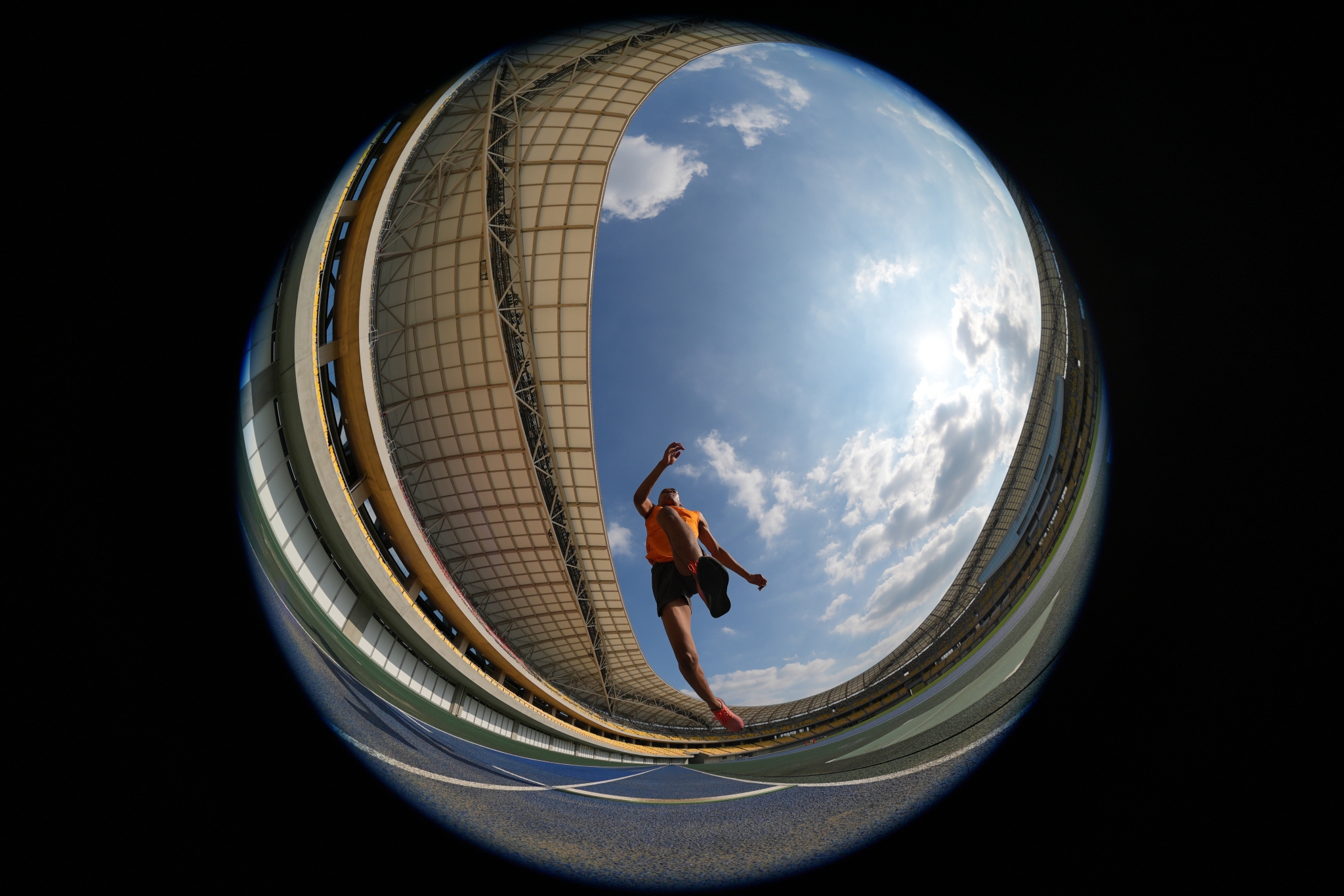 Athlete performing long jump photographed from below looking upward, captured in fisheye lens view against blue sky Click to open modal