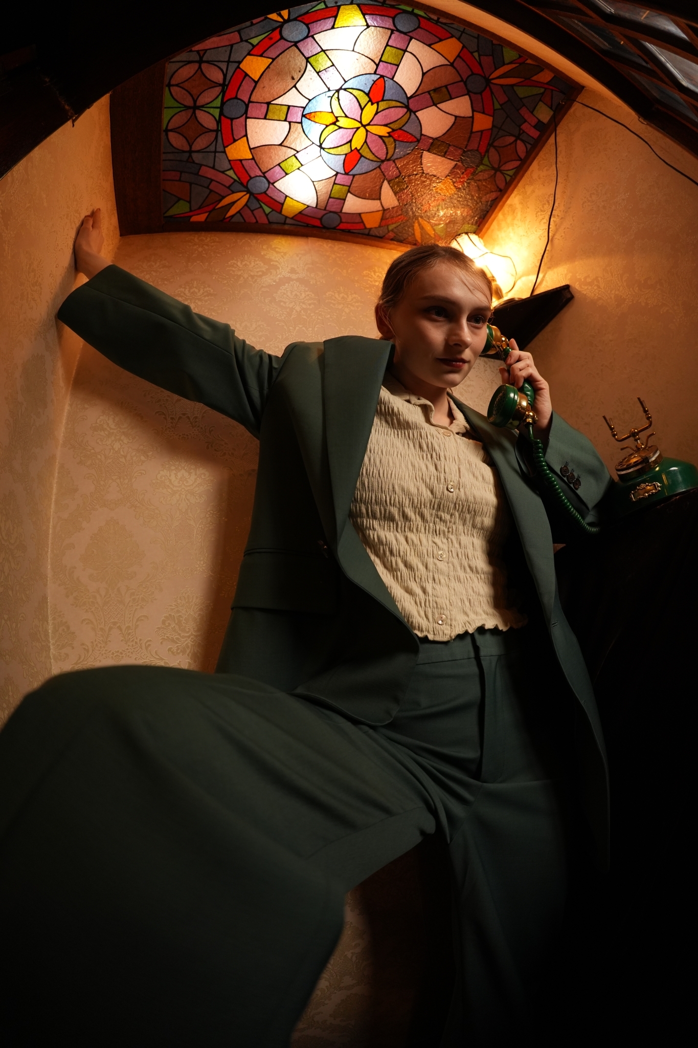 Woman in green suit posing, with warm interior lighting in background Click to open modal