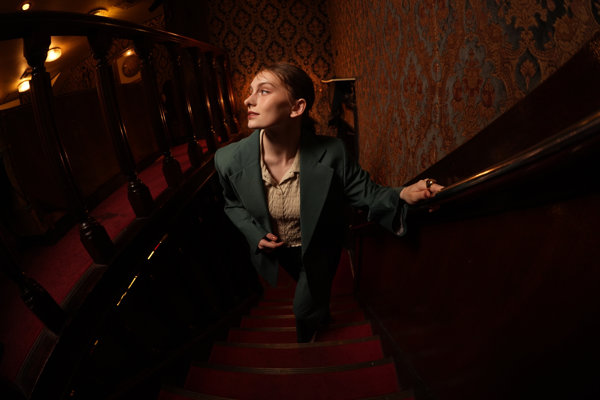 Woman in dark suit walking up stairs, illuminated by warm lighting in dimly lit room Click to open modal