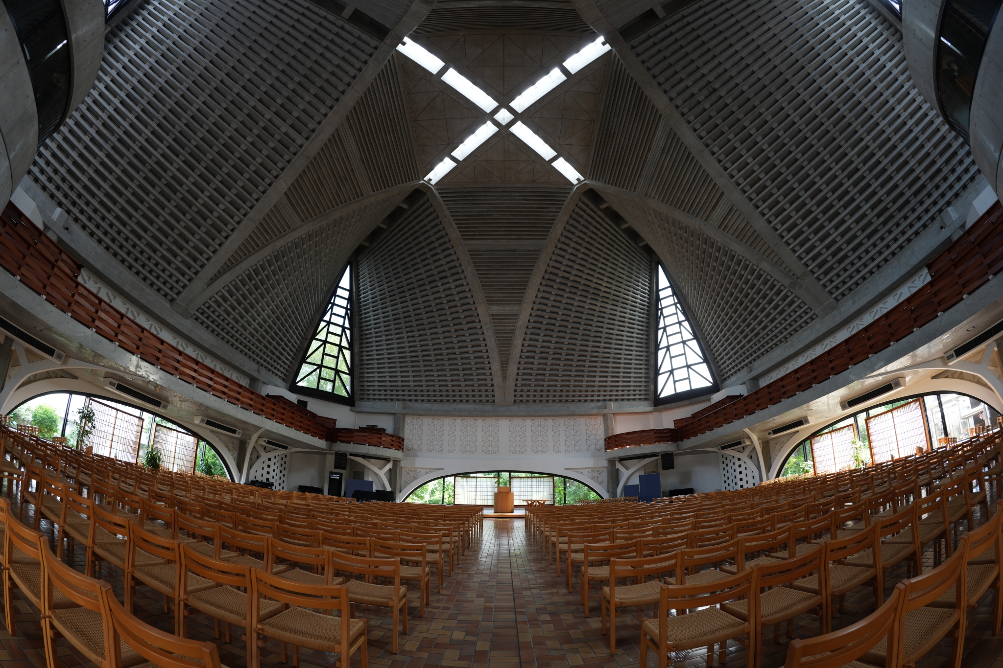 Interior of modern architecture with wooden pews, symmetrical vaulted ceiling with ribbed concrete design, and cross-shaped skylight Click to open modal