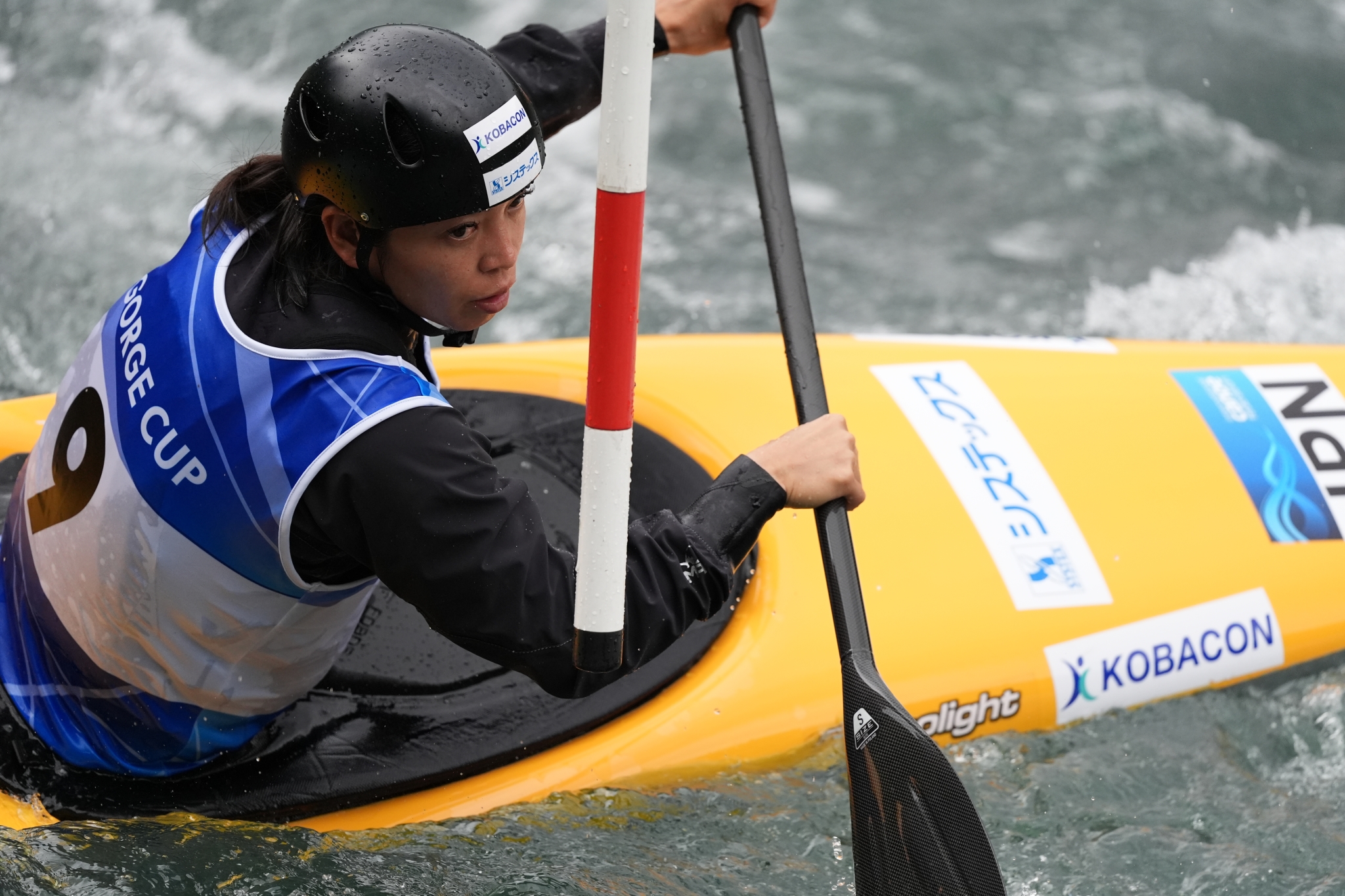 A female canoe athlete paddles through fast-moving water during a competition. Click to open modal