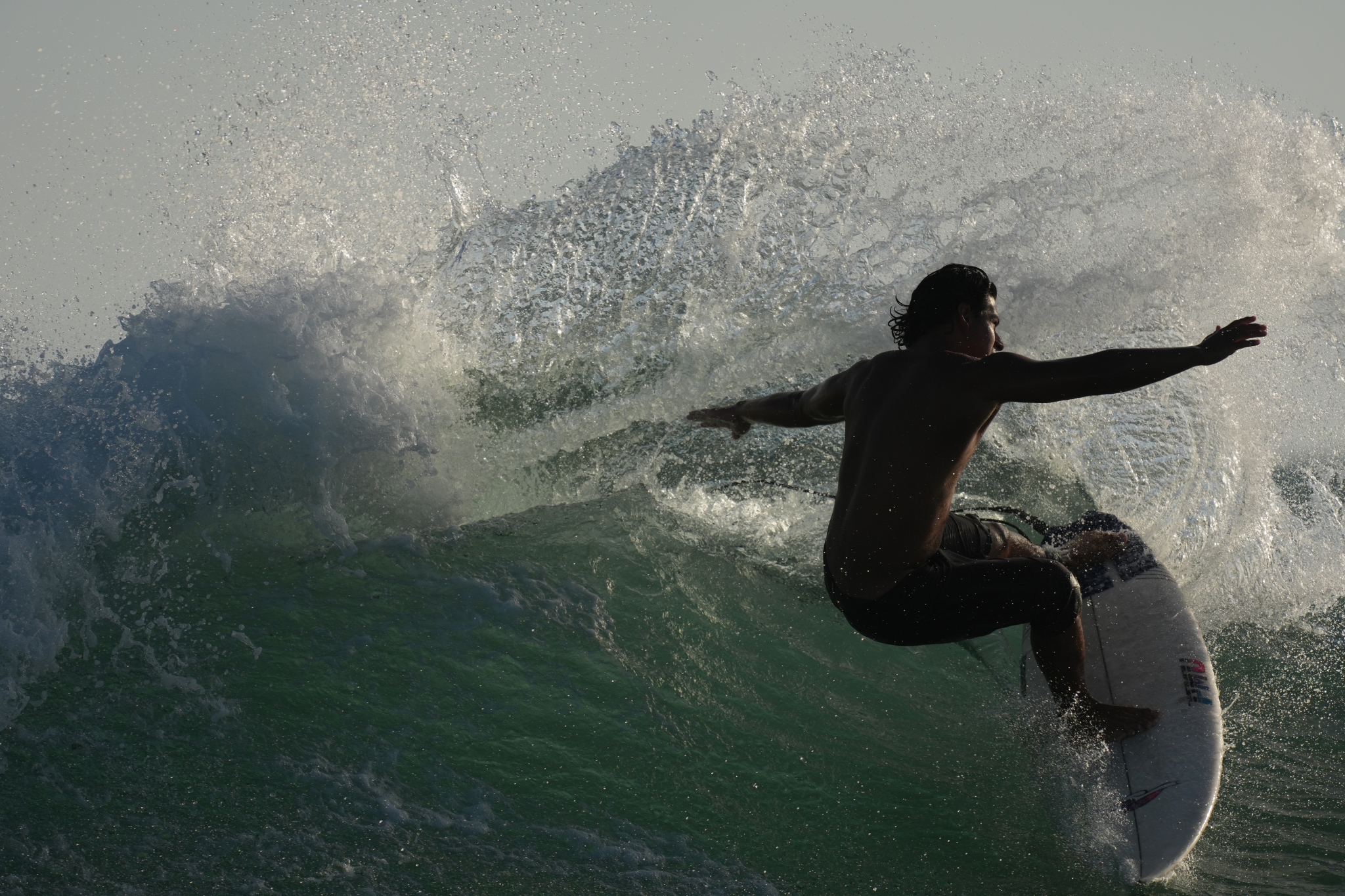 Male surfer riding through the spray of a breaking wave Click to open modal