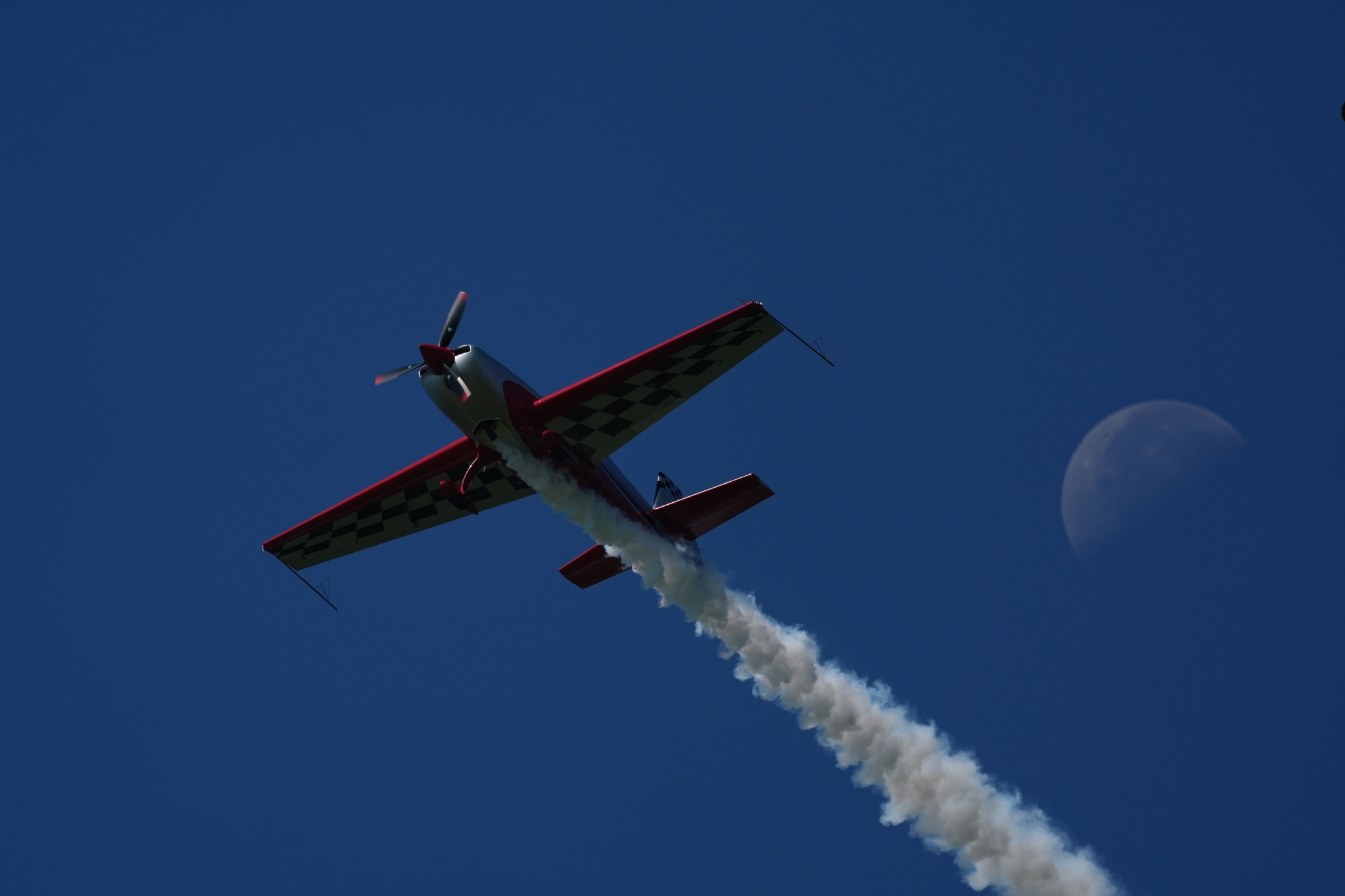 Aerobatic plane climbing past the moon with a smoke trail Click to open modal