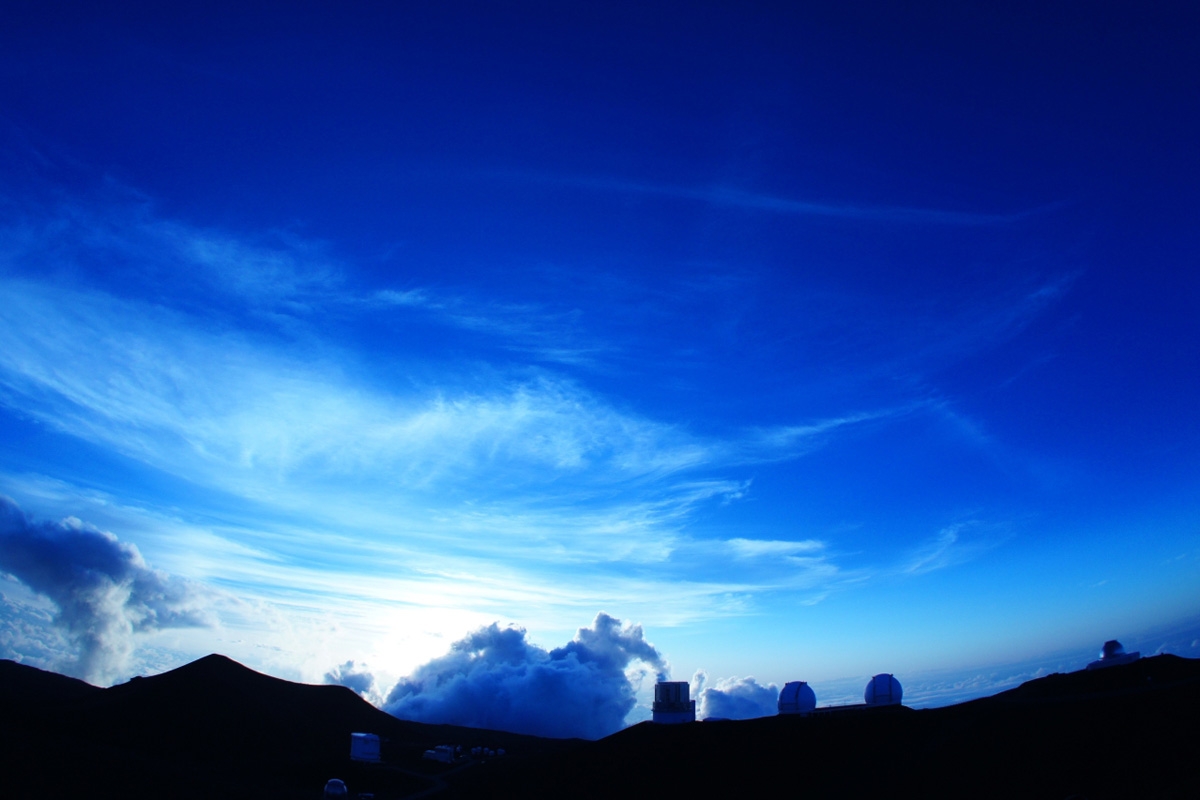 Mountain ridge with structures silhouetted against sky with low sun Click to open modal