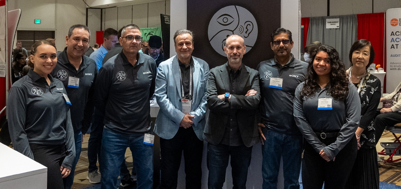 Eight members of the team are facing us with the booth in the background, looking at us with smiles on their faces.