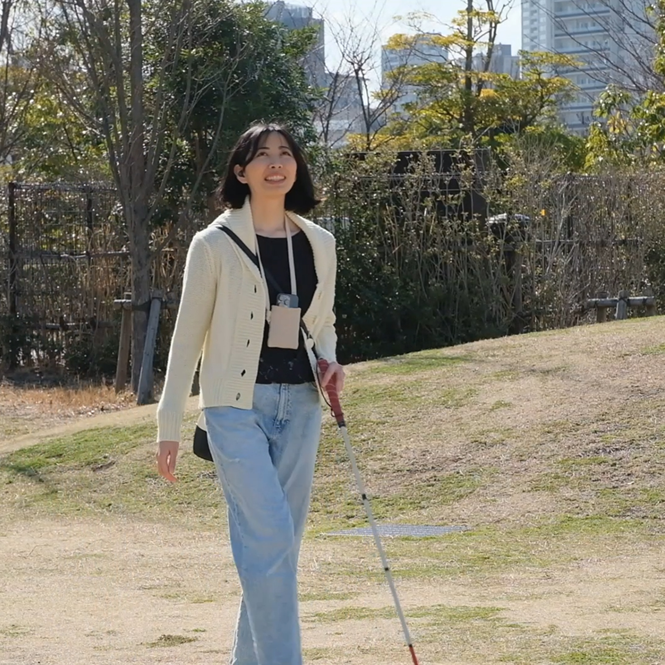 A woman is walking in the park with a white cane (safety cane for the blind).