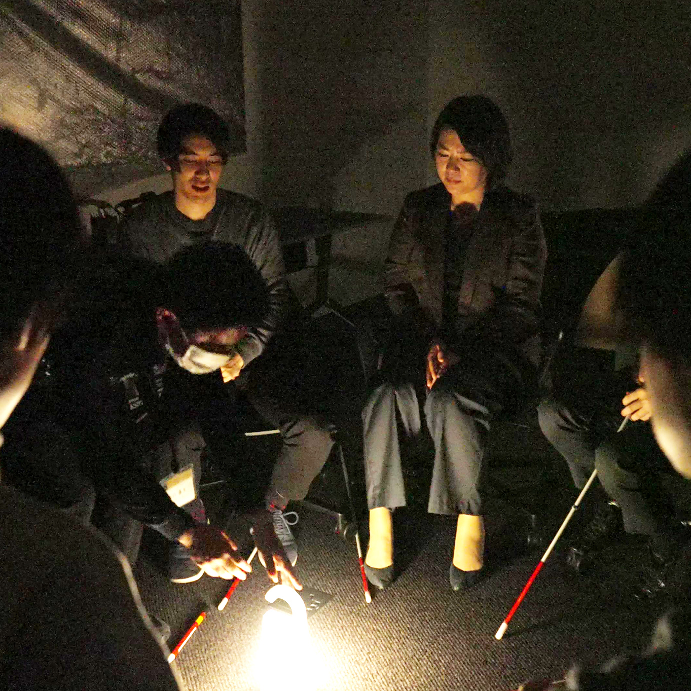 A scene from a workshop in which participants are trying to reach a predetermined goal in the dark. Participants are having an experience in a dark room.