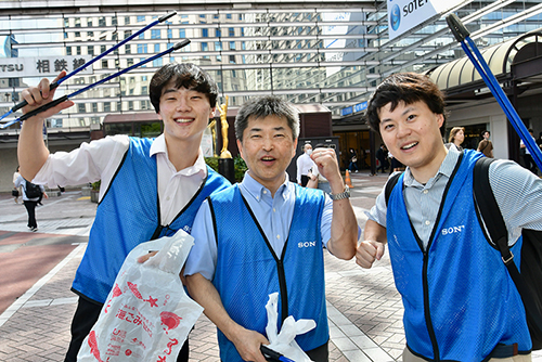 Three smiling participants picking up trash
